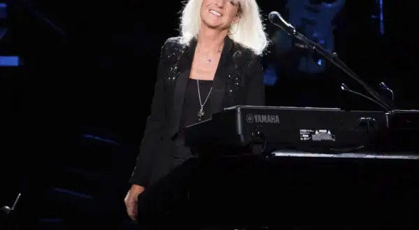 La cantante dei Fleetwood Mac, con i capelli biondi sciolti, sorride dietro una tastiera Yamaha.
