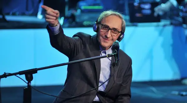 Franco Battiato, con cuffie e microfono, indica con il dito, come in un "auto da fé" di parole.