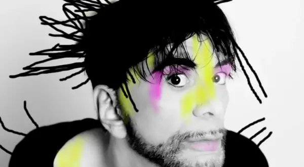 Ritratto di Ivan Cattaneo con capelli neri a punta, trucco colorato e barba. Le sue canzoni sono uniche.