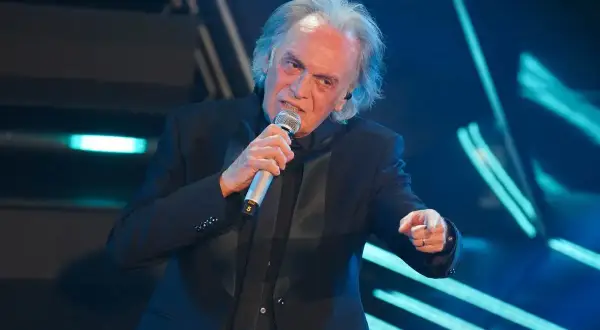 Riccardo Fogli canta sul palco, con il microfono in mano, evocando le sue indimenticabili canzoni.
