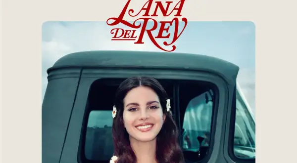 Lana Del Rey sorride, con fiori tra i capelli, accanto a un vecchio camion. Un'immagine che evoca il suo "lust for life".