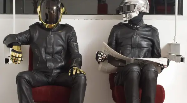 I Daft Punk, in pelle nera e caschi iconici, uno dorato e l'altro argentato, siedono leggendo il giornale.