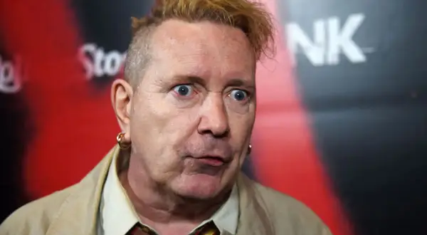 John Lydon, iconico cantante dei Sex Pistols, con un'espressione sorpresa e i capelli biondi spettinati.
