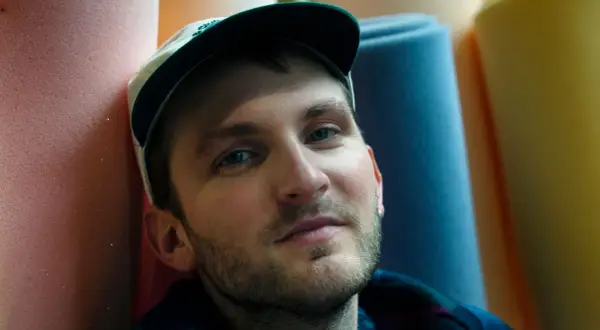 Ritratto di un uomo con cappellino, circondato da rotoli di gommapiuma colorata. Le sue canzoni di Giorgio Poi evocano immagini vivide.
