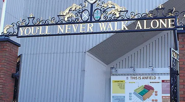 L'iconico cancello di Anfield con la scritta "You'll Never Walk Alone" e lo stemma del Liverpool. Un simbolo di unità e passione.