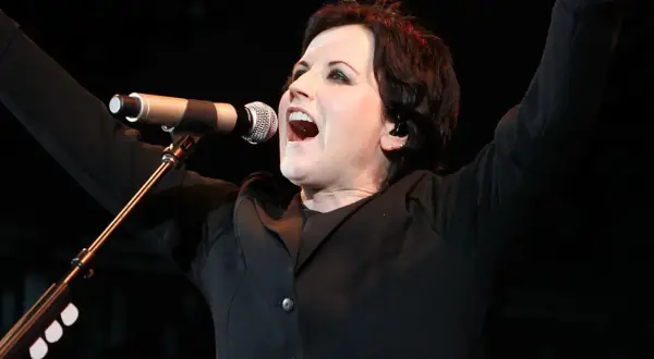 Dolores O'Riordan, iconica voce dei The Cranberries, canta con passione sul palco, braccia alzate in un momento di pura energia.