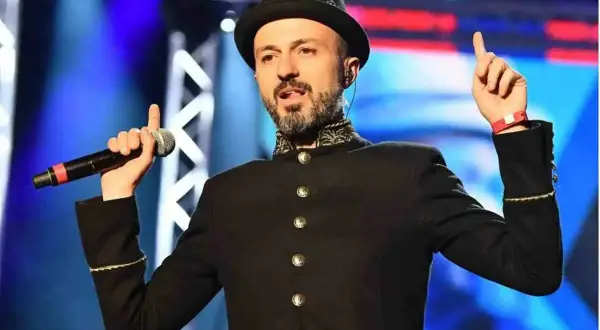 Un cantante con cappello e giacca nera, microfono in mano, evoca le canzoni dei Subsonica con un gesto energico.