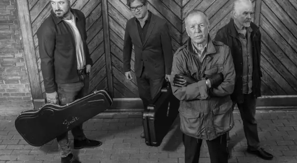 I membri di the Animals, quattro uomini con valigie per strumenti musicali, posano davanti a un portone di legno.