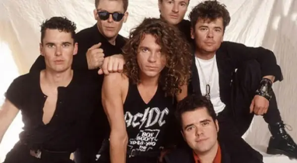I membri degli INXS posano insieme, un gruppo di sei uomini con stili diversi, pronti a conquistare il mondo con la loro musica.