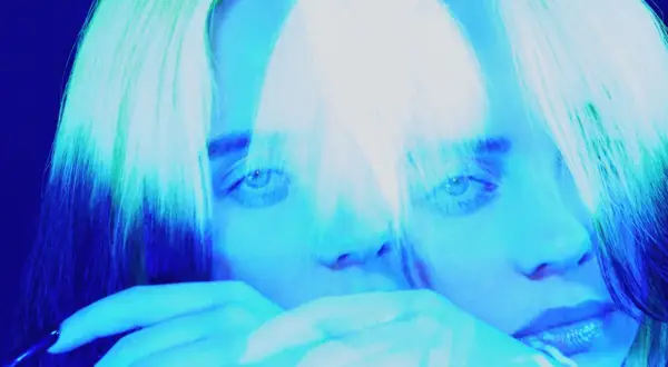Billie Eilish, icona del pop alternativo, con capelli verdi e blu, in un'immagine surreale che evoca il suo genere musicale unico.