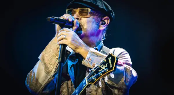 Luca Carboni canta "Le storie d'amore" con passione, chitarra in mano, sotto le luci del palco.