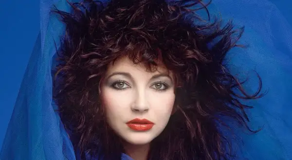 Ritratto di Kate Bush con capelli scuri e fluenti, occhi verdi penetranti e labbra rosse, avvolta in un velo blu. Un'icona delle canzoni di Kate Bush.