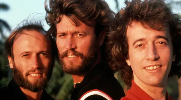 I tre fratelli Gibb dei Bee Gees, con i loro iconici capelli e sorrisi, sembrano dire "run to me" con la loro musica.