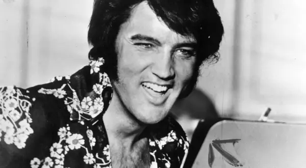 Un giovane Elvis Presley, con la sua iconica capigliatura e una camicia floreale, sorride. Un'immagine che cattura un momento della sua storia.
