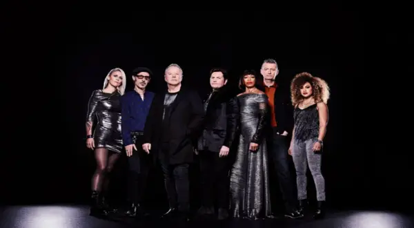 I membri dei Simple Minds posano in gruppo su sfondo nero, vestiti con abiti eleganti e scintillanti.