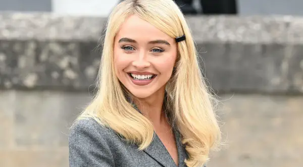 Sabrina Carpenter sorride, con i capelli biondi e un blazer grigio. Ricorda i suoi film e programmi TV.