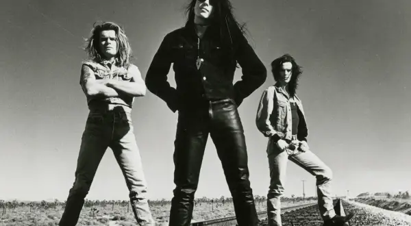 I membri dei The Cult posano sulle rotaie in un paesaggio desertico, con un cielo limpido sullo sfondo.