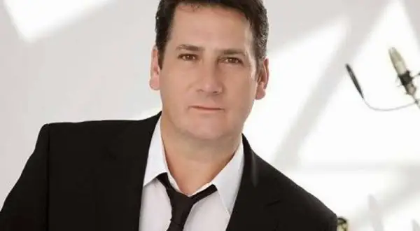 Tony Hadley, uno dei membri dei Spandau Ballet, in giacca e cravatta, con un microfono sullo sfondo.