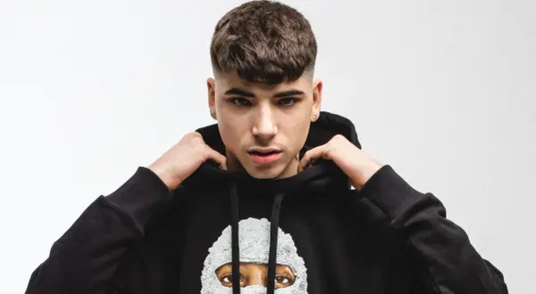 Giovane rapper italiano con un taglio di capelli alla moda, indossa una felpa nera con un disegno artistico.