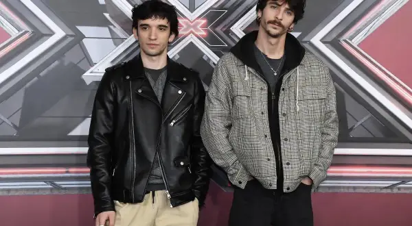 I **santi francesi** posano davanti al logo di X Factor. Uno indossa un chiodo di pelle nera, l'altro una giacca a quadri.