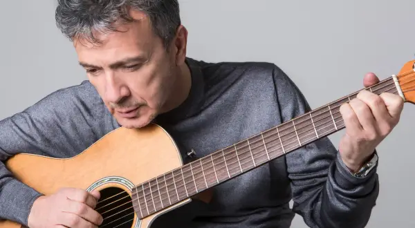 Uomo con chitarra acustica, intento a suonare, forse componendo nuove canzoni di pupo.