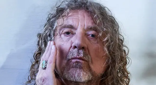 Primo piano di Robert Plant, con la mano sul viso, un anello turchese. La sua espressione è intensa, quasi una saving grace per chi lo osserva.