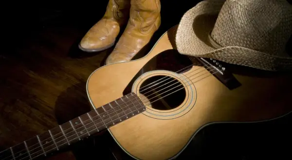 Stivali da cowboy, cappello di paglia e chitarra acustica, pronti per suonare le più belle canzoni country famose.