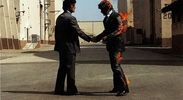 Due uomini si stringono la mano, uno in fiamme. Un'immagine iconica che evoca il "wish you were here significato" di assenza e desiderio.