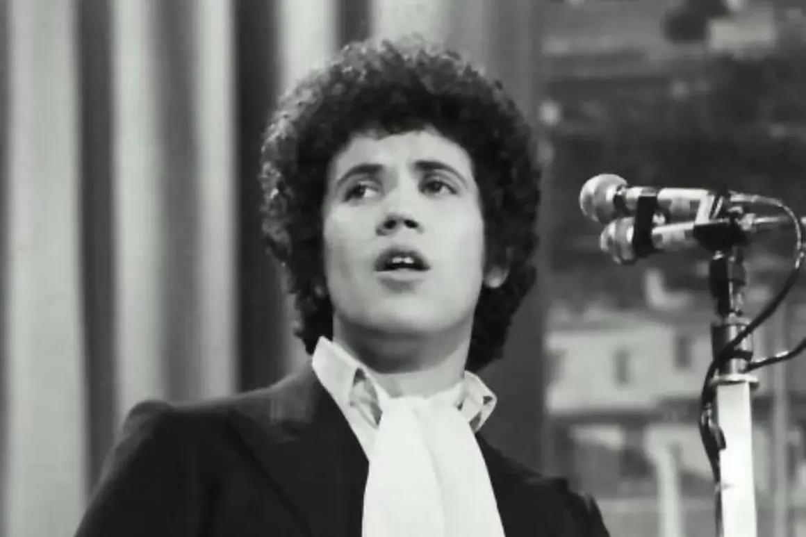 Lucio Battisti, con la sua iconica chioma, canta "Il tempo di morire" davanti a un microfono.