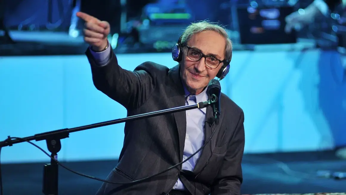 Franco Battiato, con cuffie e microfono, indica con il dito, come in un "auto da fé" di parole.