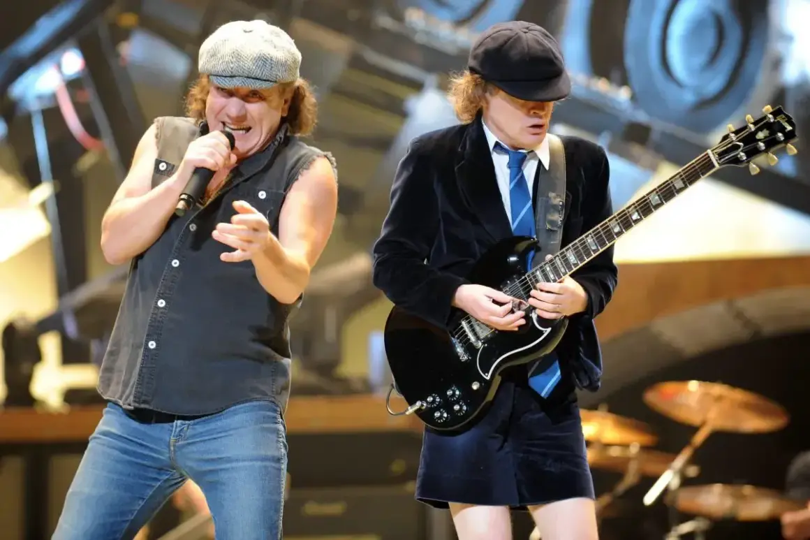 Brian Johnson canta con passione mentre Angus Young suona la chitarra, iconici membri degli AC/DC in pieno concerto.