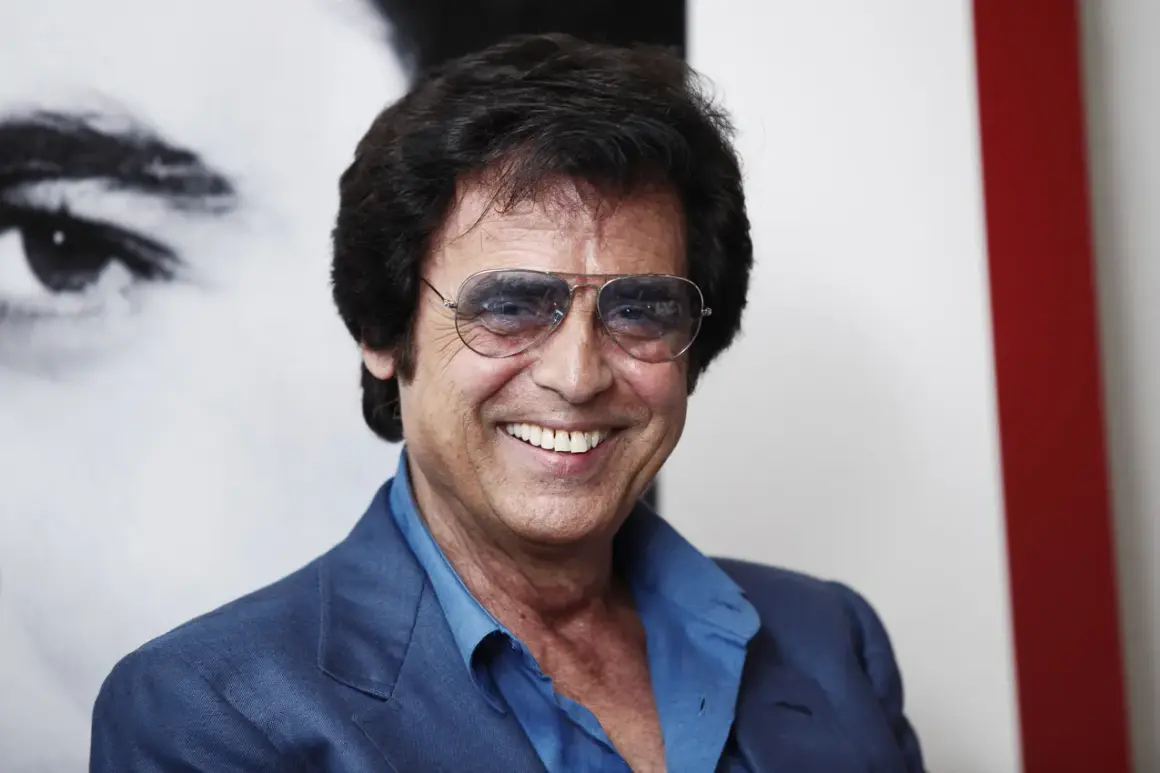 Un uomo sorridente con occhiali da sole aviator, indossa una giacca blu. Potrebbe essere Little Tony, pronto a cantare le sue canzoni.
