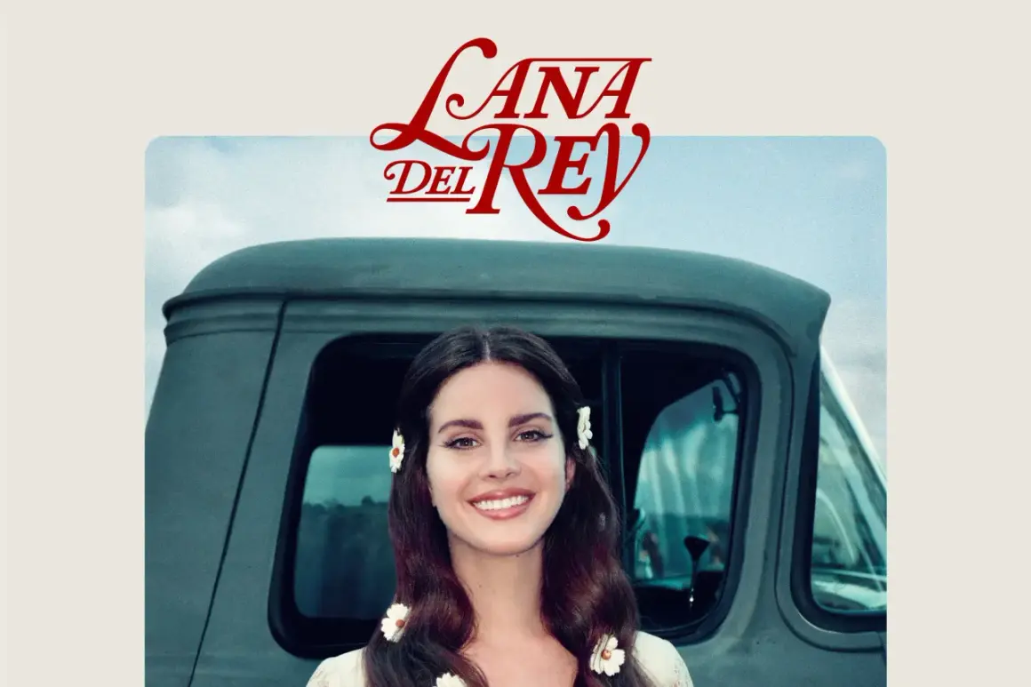 Lana Del Rey sorride, con fiori tra i capelli, accanto a un vecchio camion. Un'immagine che evoca il suo "lust for life".
