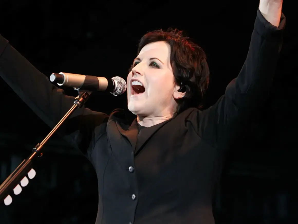 Dolores O'Riordan, iconica voce dei The Cranberries, canta con passione sul palco, braccia alzate in un momento di pura energia.