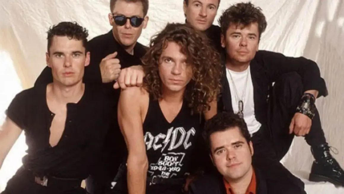 I membri degli INXS posano insieme, un gruppo di sei uomini con stili diversi, pronti a conquistare il mondo con la loro musica.