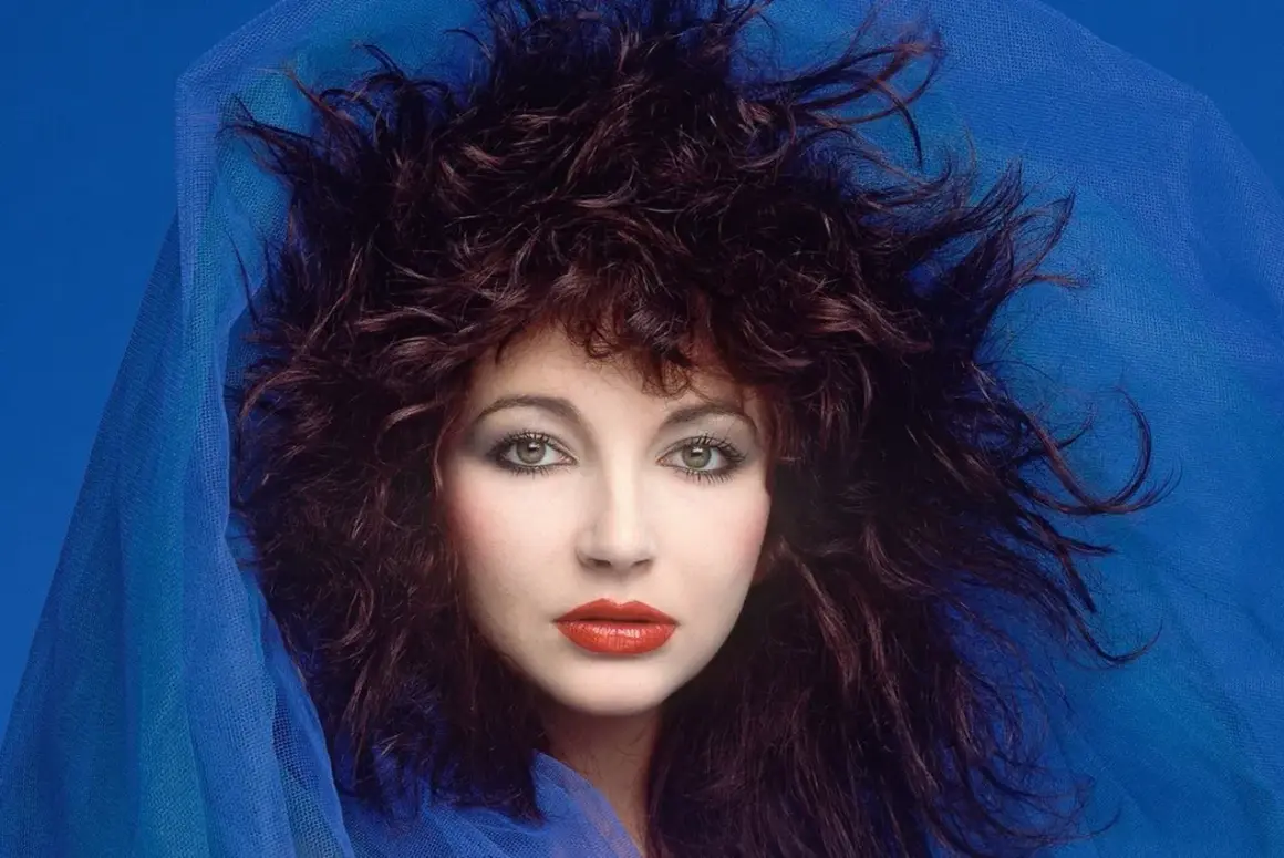 Ritratto di Kate Bush con capelli scuri e fluenti, occhi verdi penetranti e labbra rosse, avvolta in un velo blu. Un'icona delle canzoni di Kate Bush.