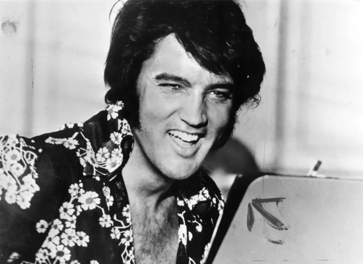 Un giovane Elvis Presley, con la sua iconica capigliatura e una camicia floreale, sorride. Un'immagine che cattura un momento della sua storia.