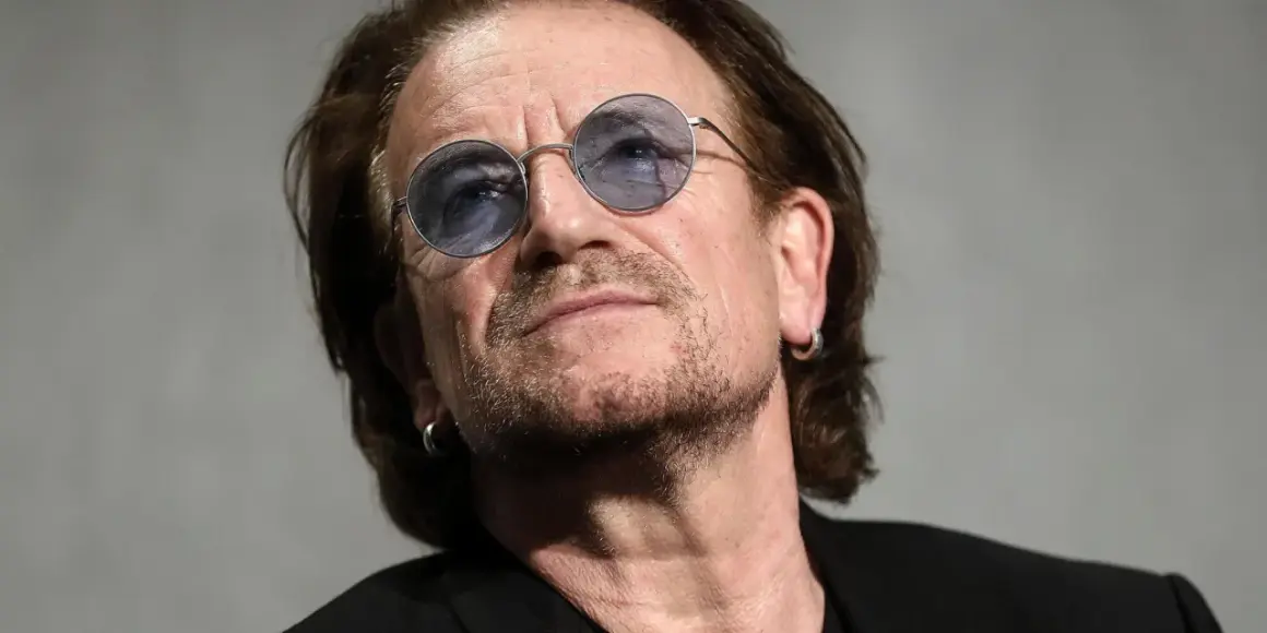 Primo piano di Bono Vox con occhiali rotondi blu, che ricorda le sue iconiche canzoni.