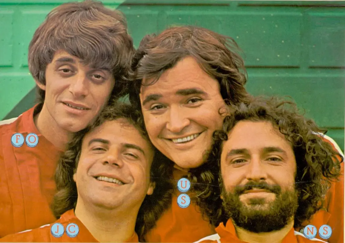 I gatti di Vicolo Miracoli sorridono alla telecamera, un gruppo di amici con capelli mossi e barbe folte.