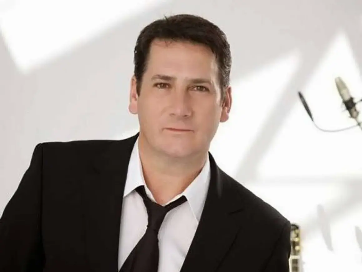 Tony Hadley, uno dei membri dei Spandau Ballet, in giacca e cravatta, con un microfono sullo sfondo.