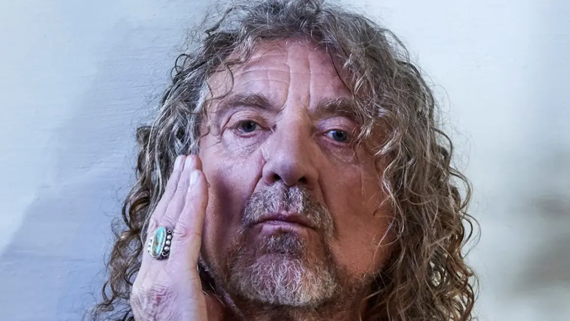 Primo piano di Robert Plant, con la mano sul viso, un anello turchese. La sua espressione è intensa, quasi una saving grace per chi lo osserva.