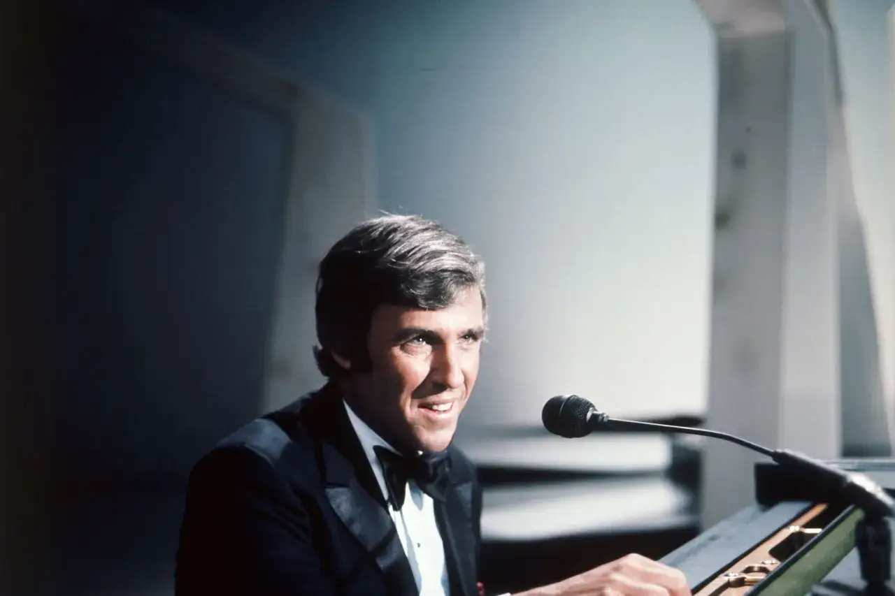 Burt Bacharach, sorridente in smoking, pronto a dirigere le sue indimenticabili canzoni.