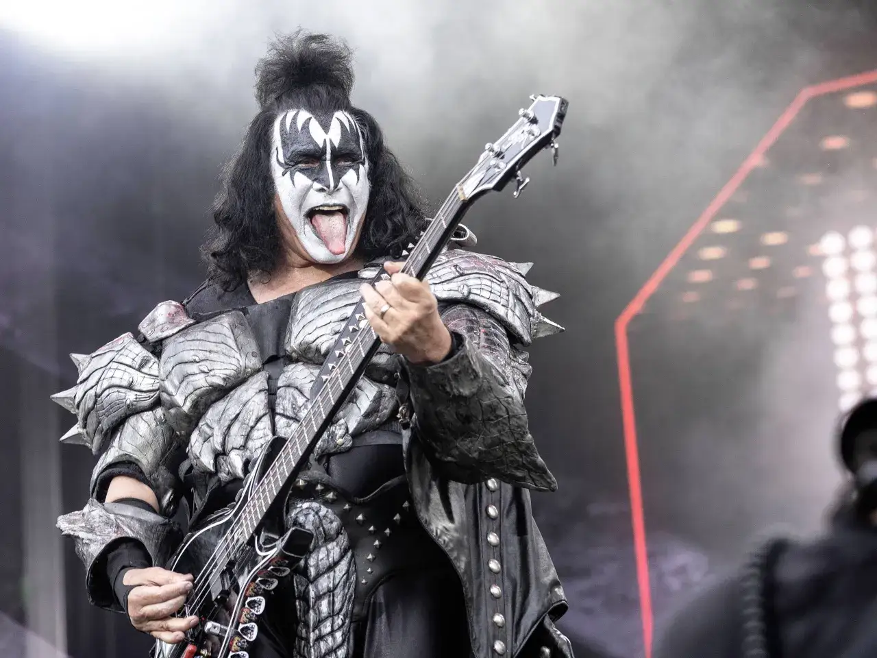 Gene Simmons dei Kiss band rock con trucco demoniaco e costume da armatura suona il basso sul palco.