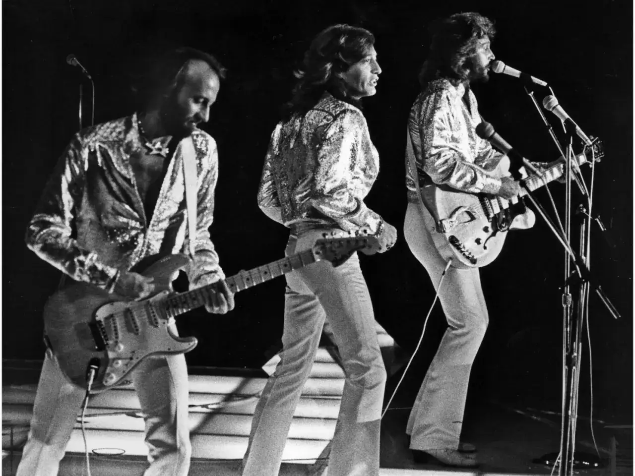 I fratelli Gibb dei Bee Gees, con le loro iconiche camicie scintillanti, suonano le loro canzoni dal vivo.