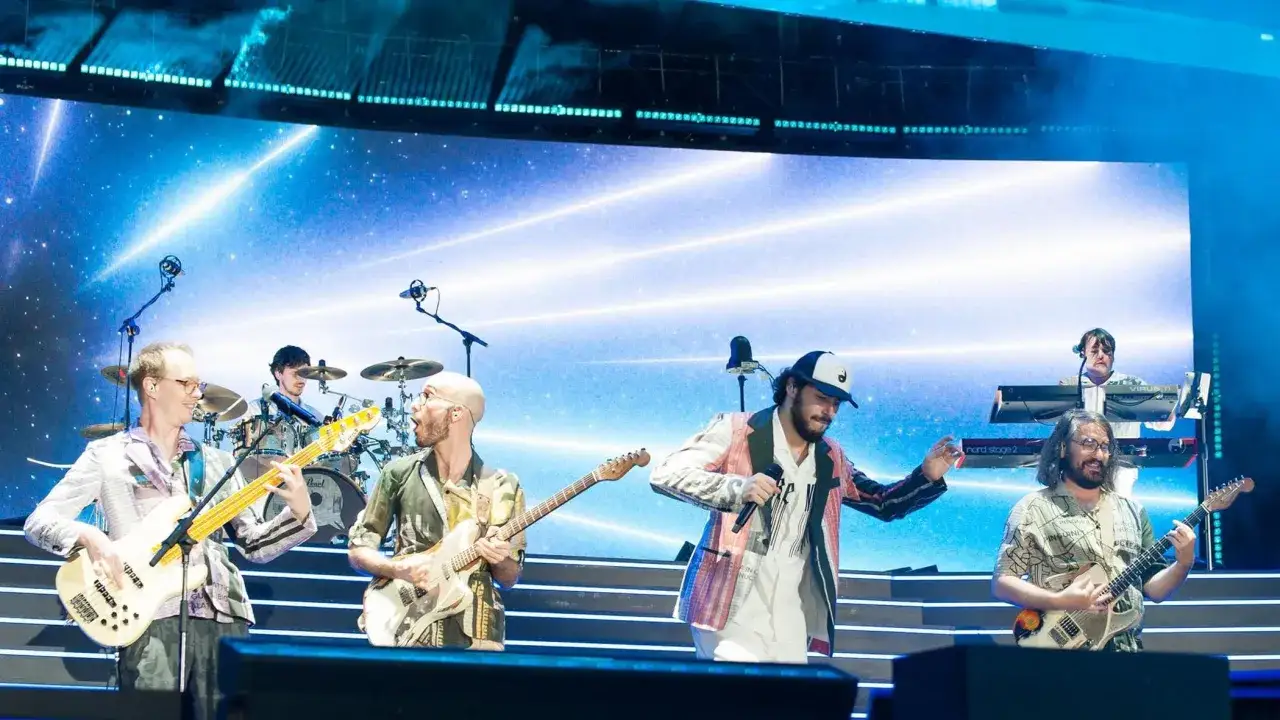 I Pinguini Tattici Nucleari sul palco, con luci stellari sullo sfondo. La band suona con energia, creando un'atmosfera vibrante.
