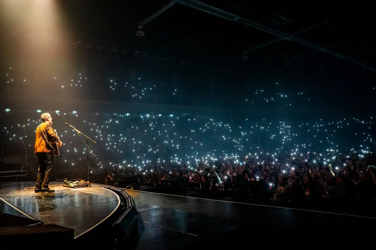 Brunori Sas sul palco, illuminato da un fascio di luce, mentre il pubblico alza i cellulari creando un mare di stelle.