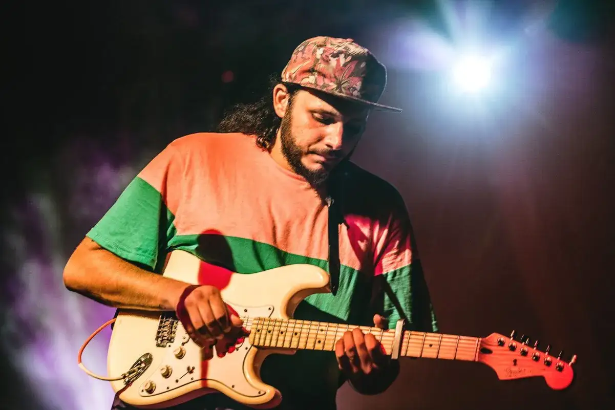 Chitarrista con cappellino floreale e maglia color block, concentrato sulla sua Fender. Chiunque pensi sia sbagliato su di lui, si sbaglia.