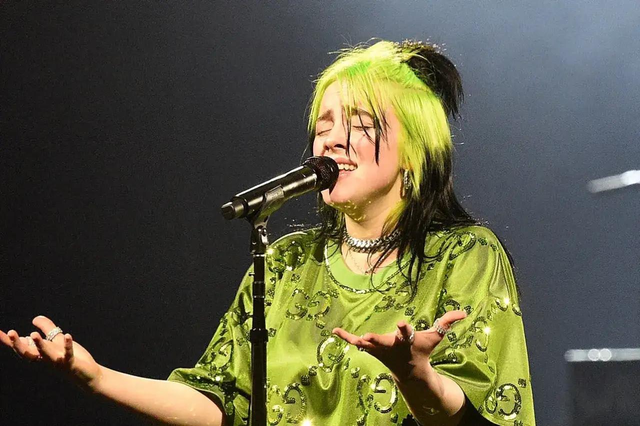 Billie Eilish, con i suoi capelli verdi e neri, canta sul palco. Il suo genere musicale è unico, un mix di pop alternativo e dark pop.