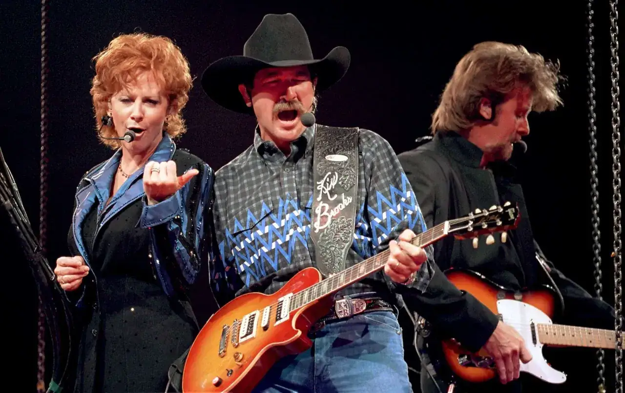 Reba McEntire, Garth Brooks e un altro musicista sul palco, interpretando canzoni country famose.