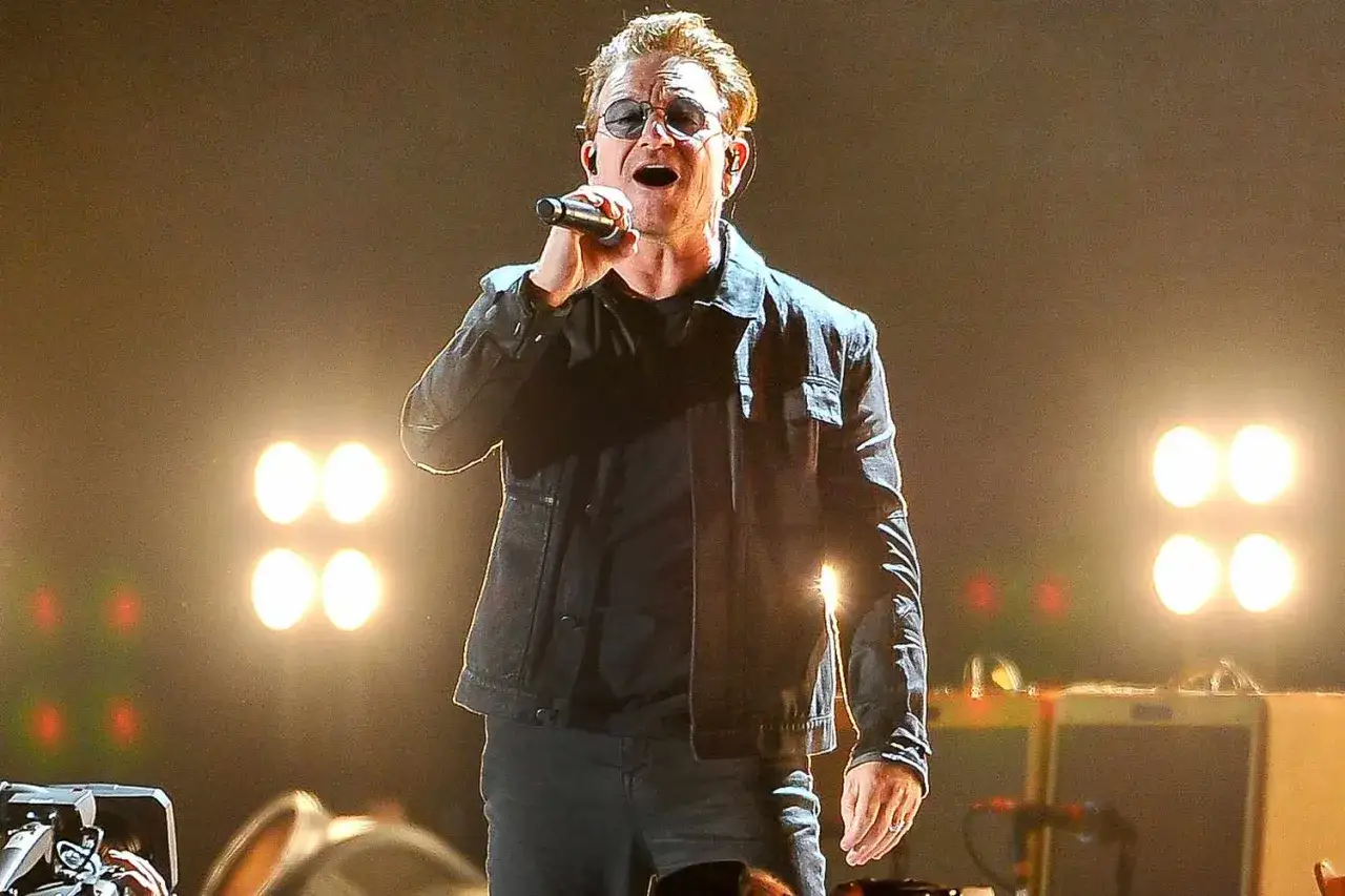 Bono Vox canta sul palco, illuminato da luci intense, mentre esegue le sue canzoni.